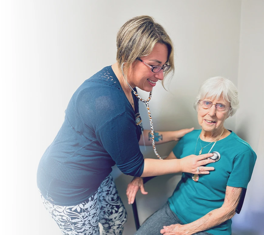 Female healthcare provider using a stethoscope to check the heart of an elderly woman who is smiling